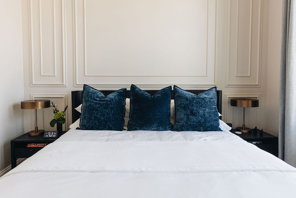 Bedroom with white bedding, navy pillows, black nightstands, and gold lamps.