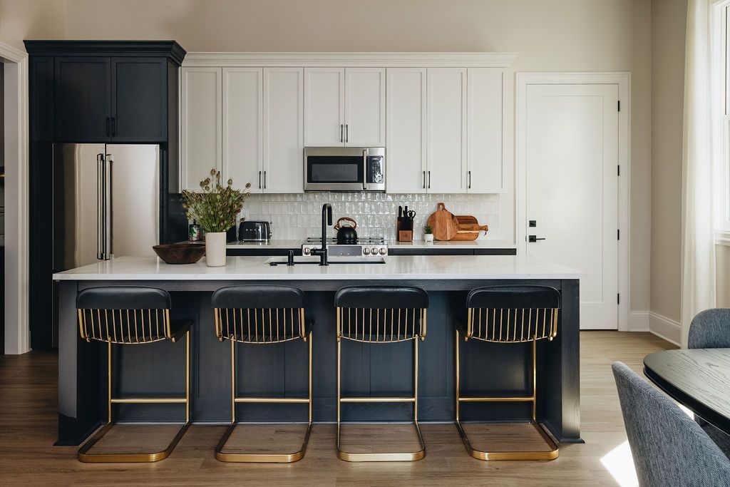 Modern kitchen with navy and white cabinets, island with gold barstools, and stainless steel appliances. Purple Martin Hotel