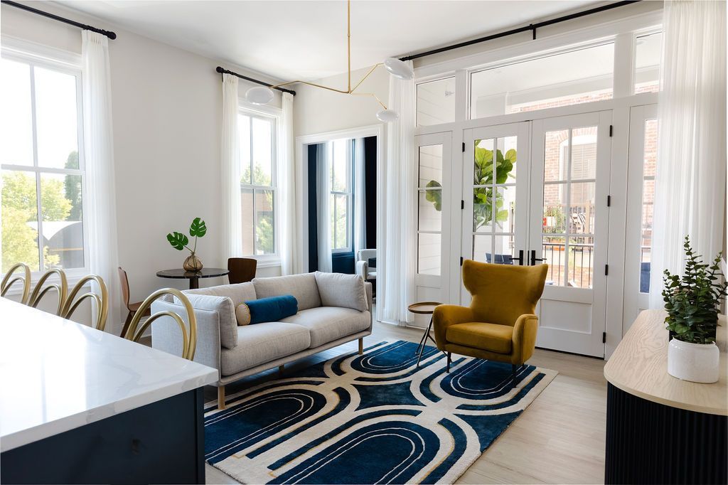 Living room with white walls, large windows, and blue and gold decor, including a rug and sofa.