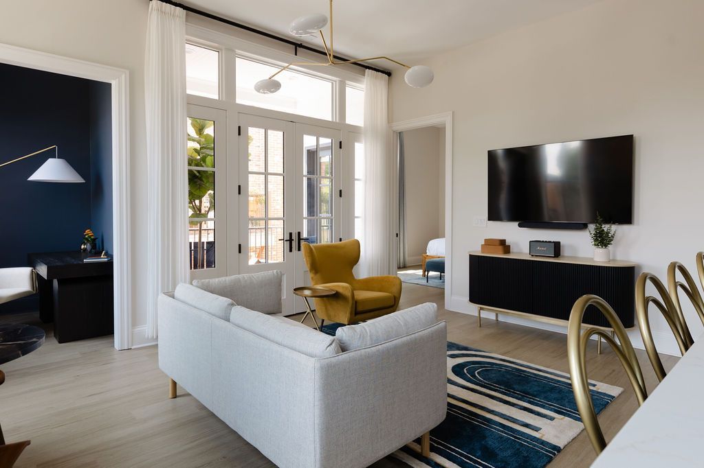 Living room with white walls, a gray sofa, yellow armchair, and a large TV over a black cabinet. Purple Martin Hotel