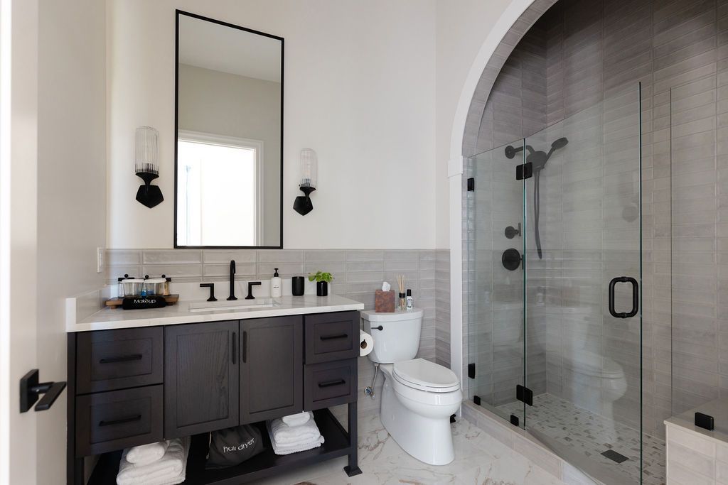 Bathroom with dark vanity, black framed mirror, glass shower, and white tile.