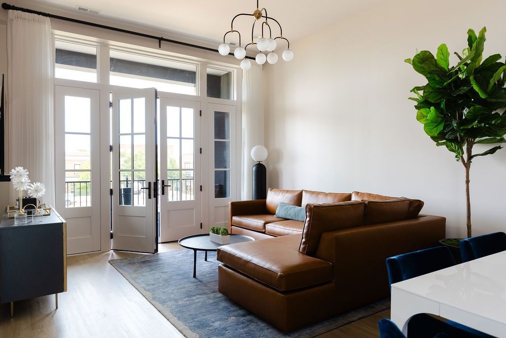 Living room with brown leather sectional, French doors, and a fiddle leaf fig. Purple Martin Hotel