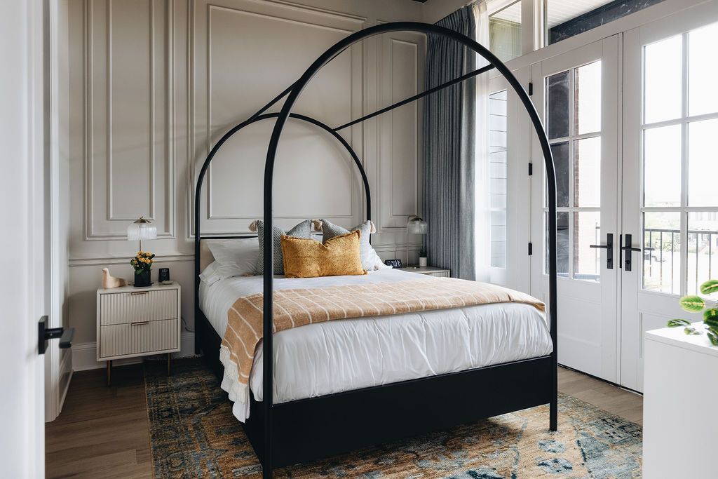 Bedroom with black canopy bed, white bedding, and ornate wall paneling. Purple Martin Hotel