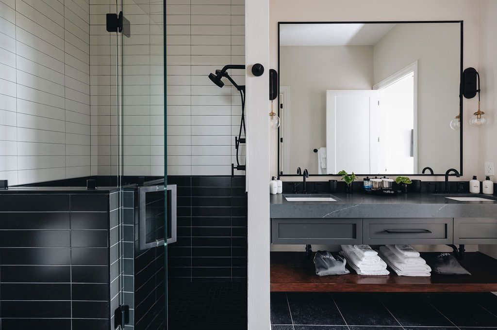 Modern bathroom with black tiled shower and vanity, glass shower door, large mirror, and open shelving. Purple Martin Hotel