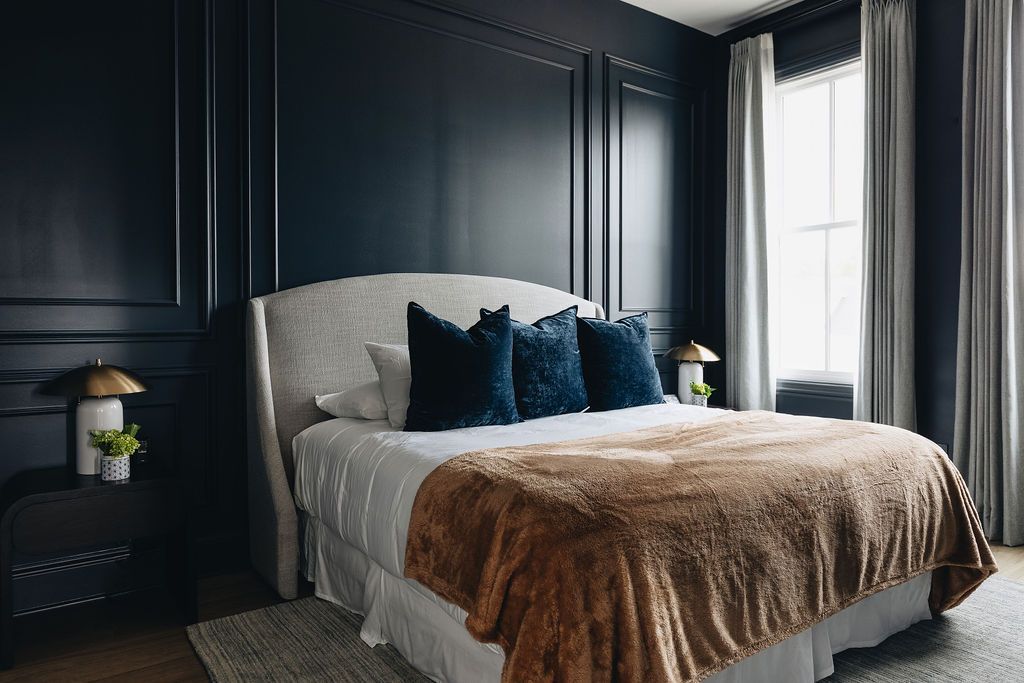Dark blue bedroom with bed, nightstand, window, and patterned wall. Purple Martin Hotel