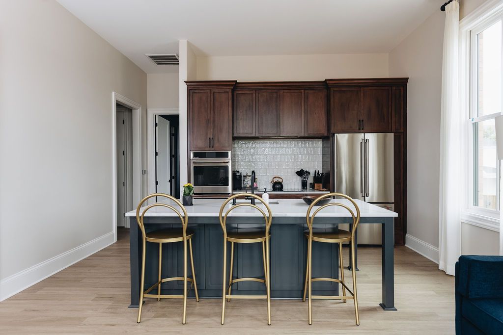 Kitchen with blue island, gold stools, dark wood cabinets, stainless steel appliances, and white walls. Purple Martin Hotel