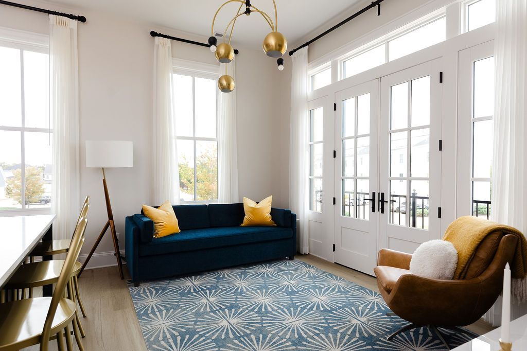 Bright living room with blue couch, rug, and windows. Brown chair, yellow throw, and gold chandelier. Purple Martin Hotel