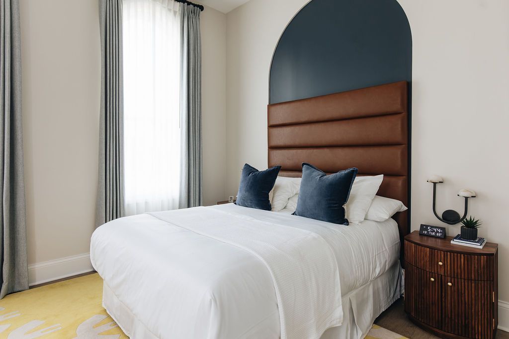 Bedroom with a bed, leather headboard, blue pillows, and wooden bedside table. Purple Martin Hotel