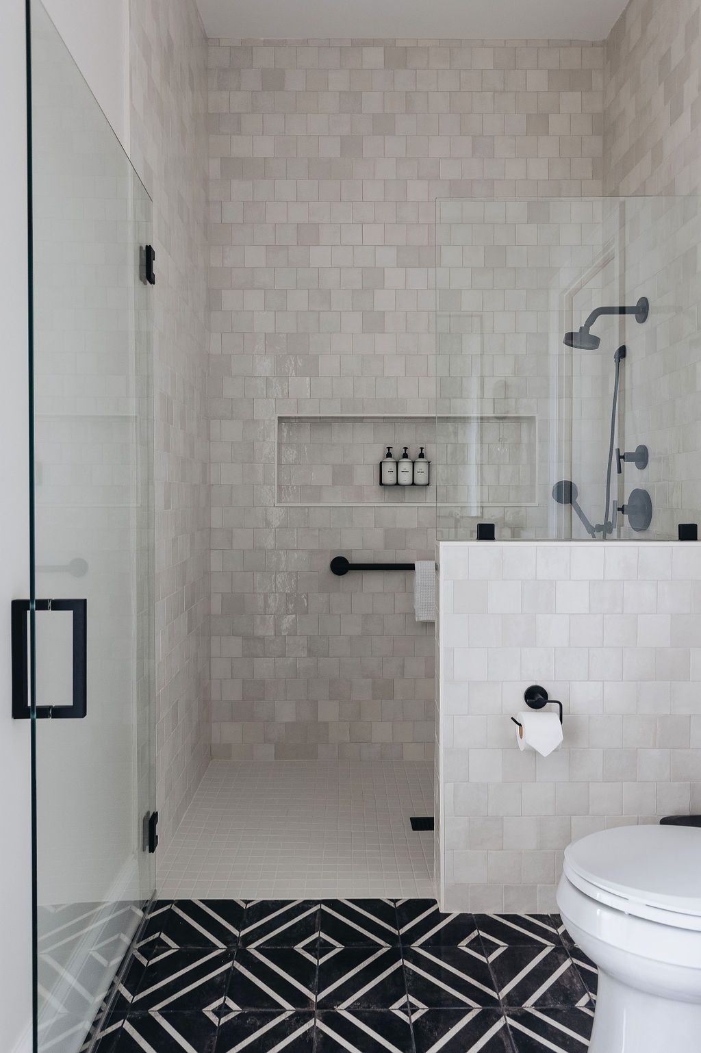 Modern bathroom with glass shower, tile walls, and black and white patterned floor.