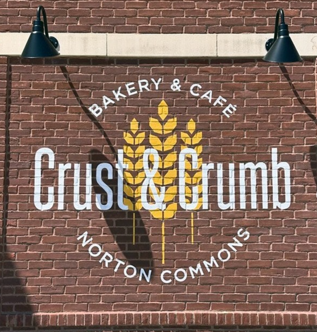 Sign for Crust & Crumb Bakery & Cafe at Norton Commons on a brick wall with wheat design.