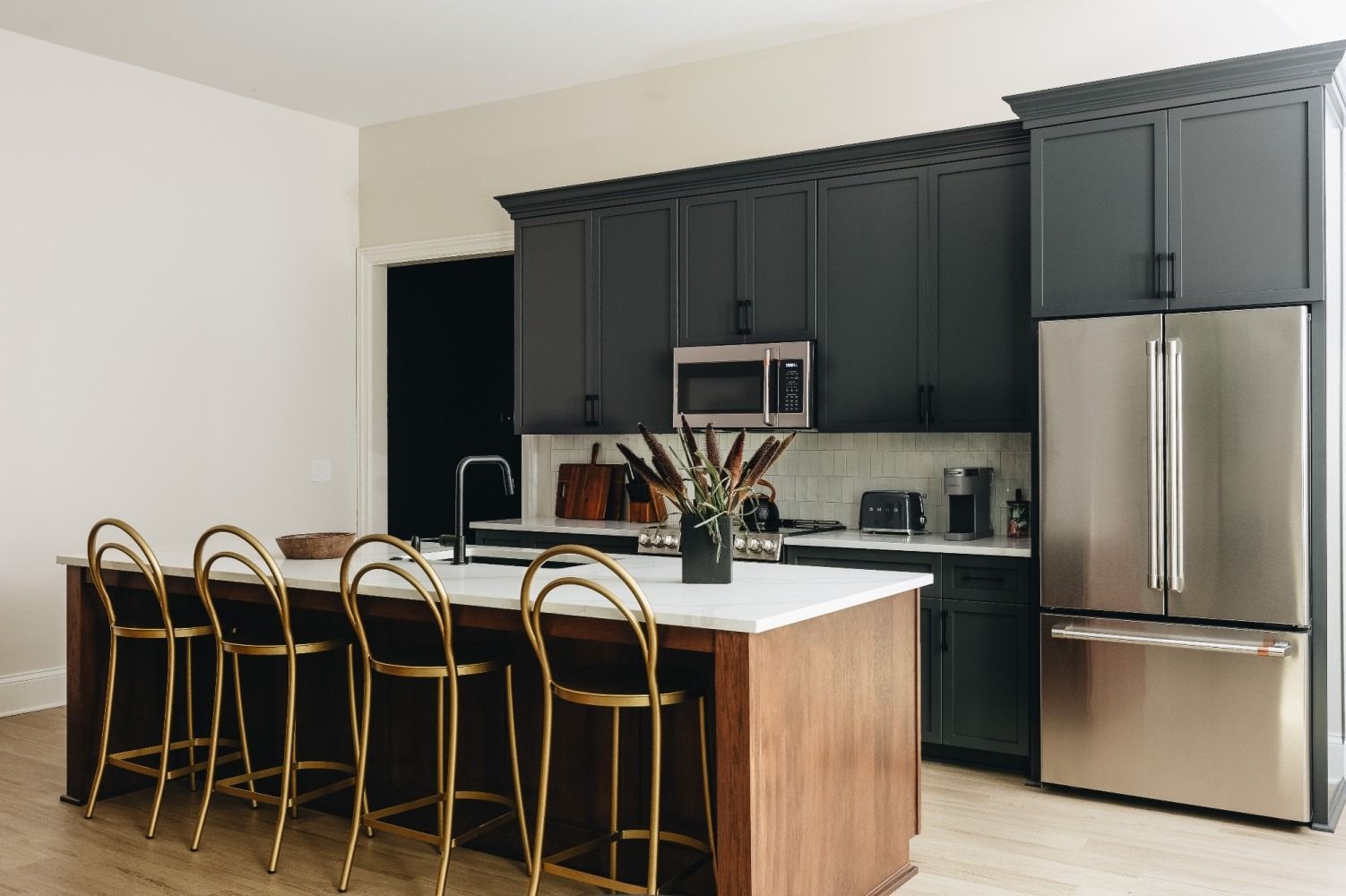 Modern kitchen with dark gray cabinets, stainless steel fridge, island with gold stools, and light countertops. Purple Martin Hotel
