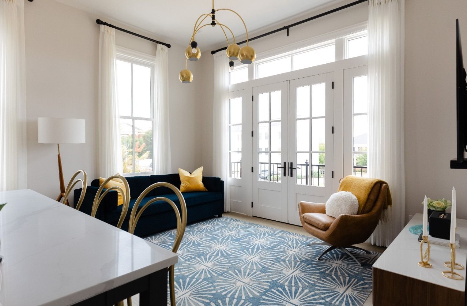 Room with blue sofa, leather chair, blue rug, French doors, and gold chandelier. Purple Martin Hotel