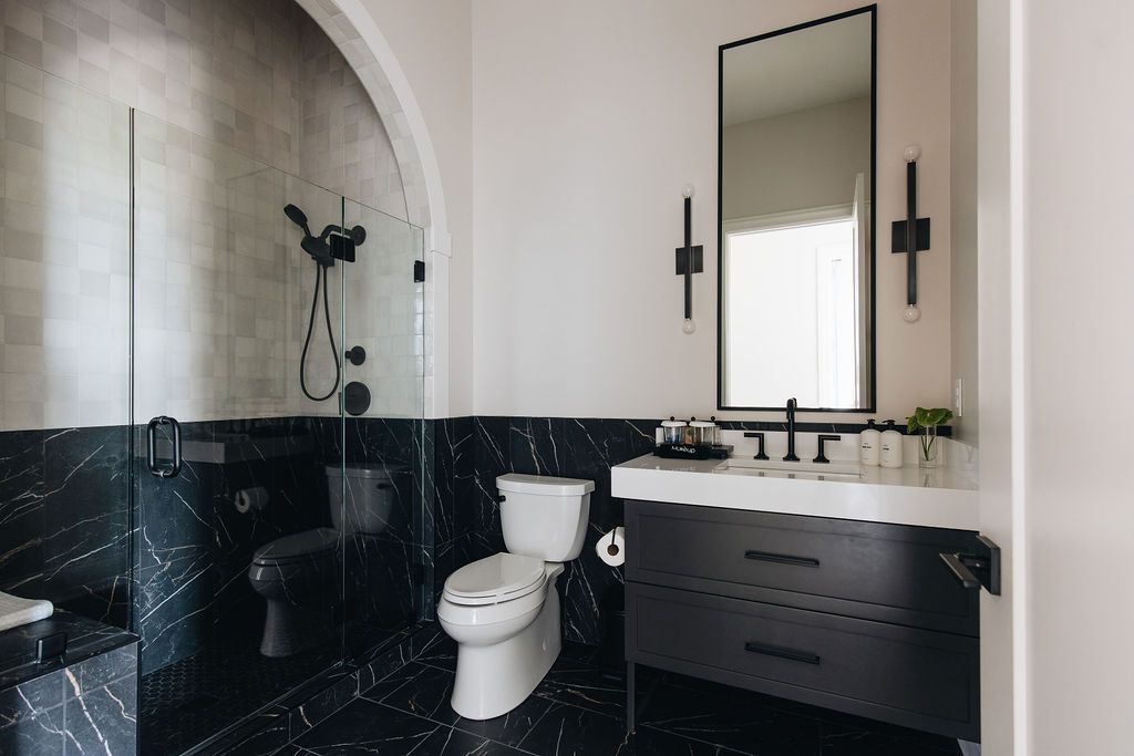 Modern black and white bathroom with marble tile, a glass shower, and a black vanity. Purple Martin Hotel