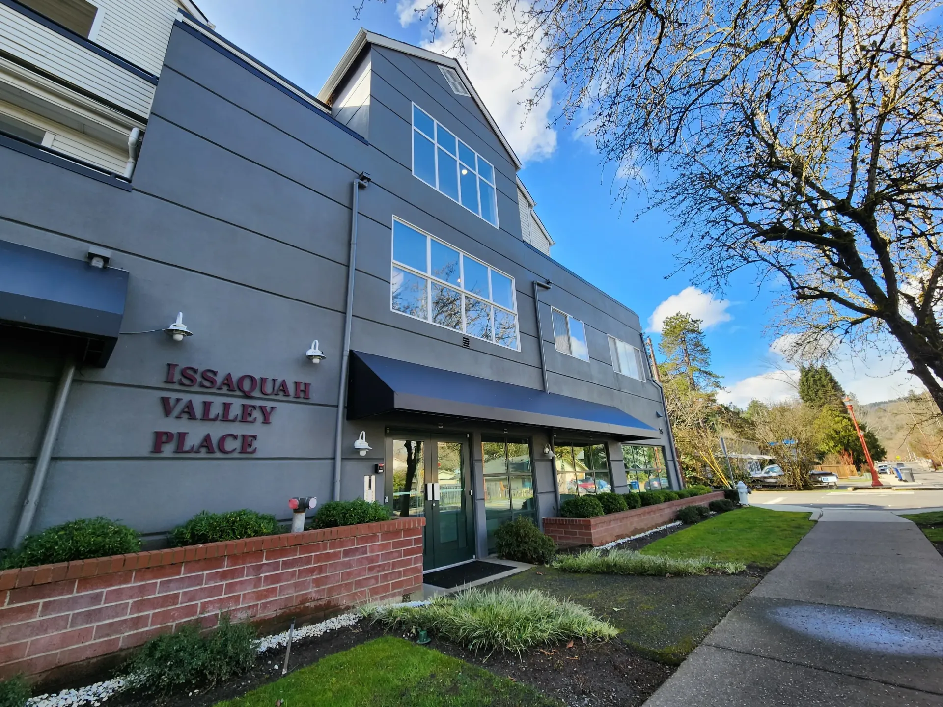 Issaquah Valley Place building with dark awnings and a brick facade, green lawn, and a sidewalk.