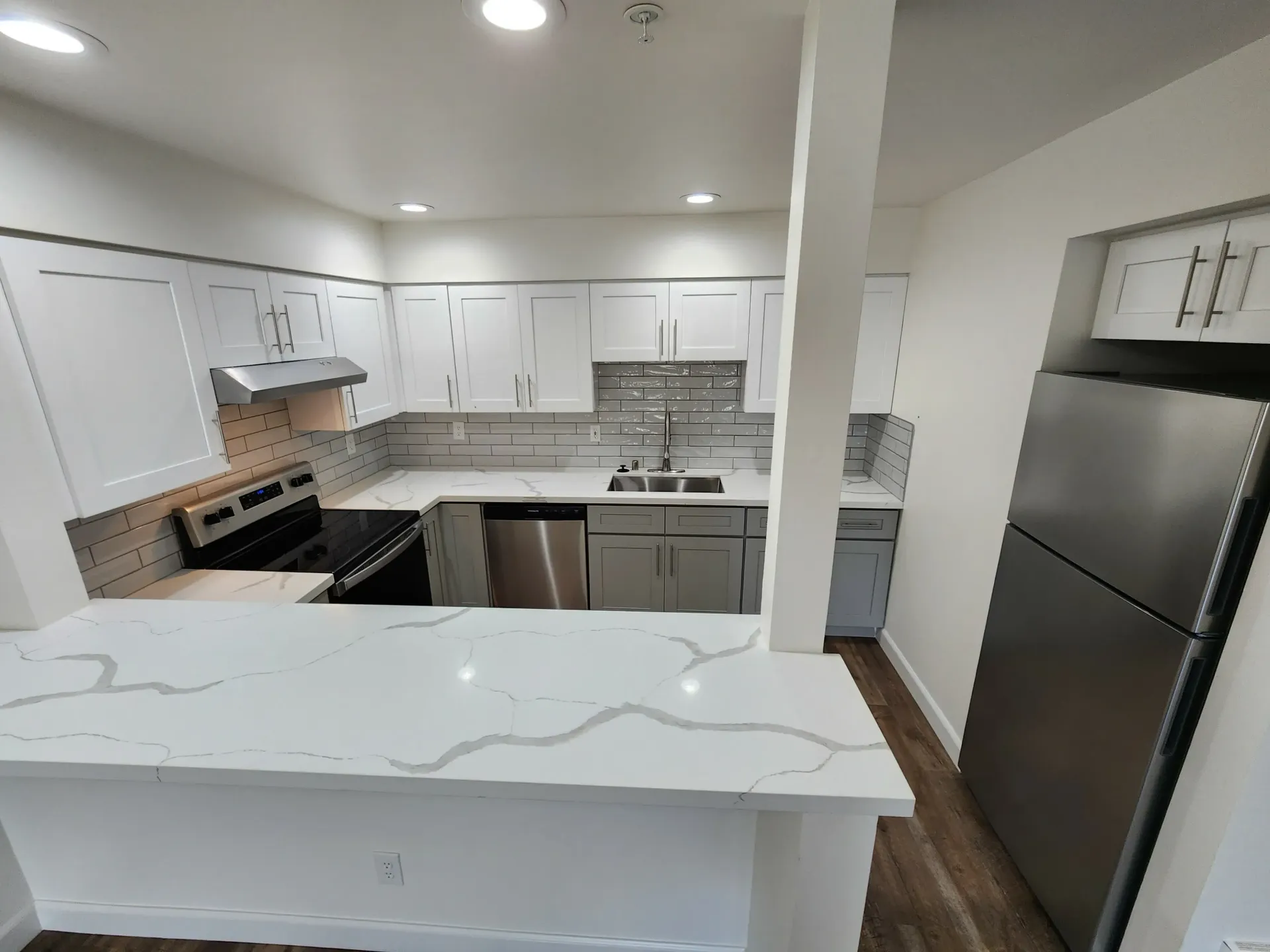 Modern kitchen with white cabinets, quartz countertops, stainless steel appliances.