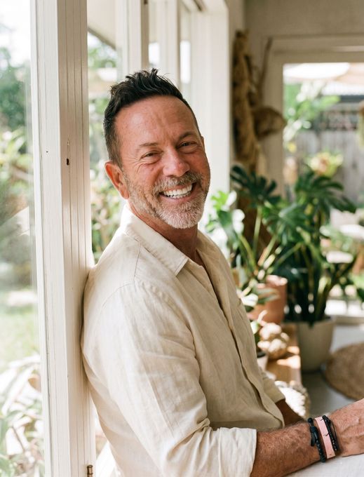 Smiling man in a light beige jacket standing in a sunlit room with potted plants