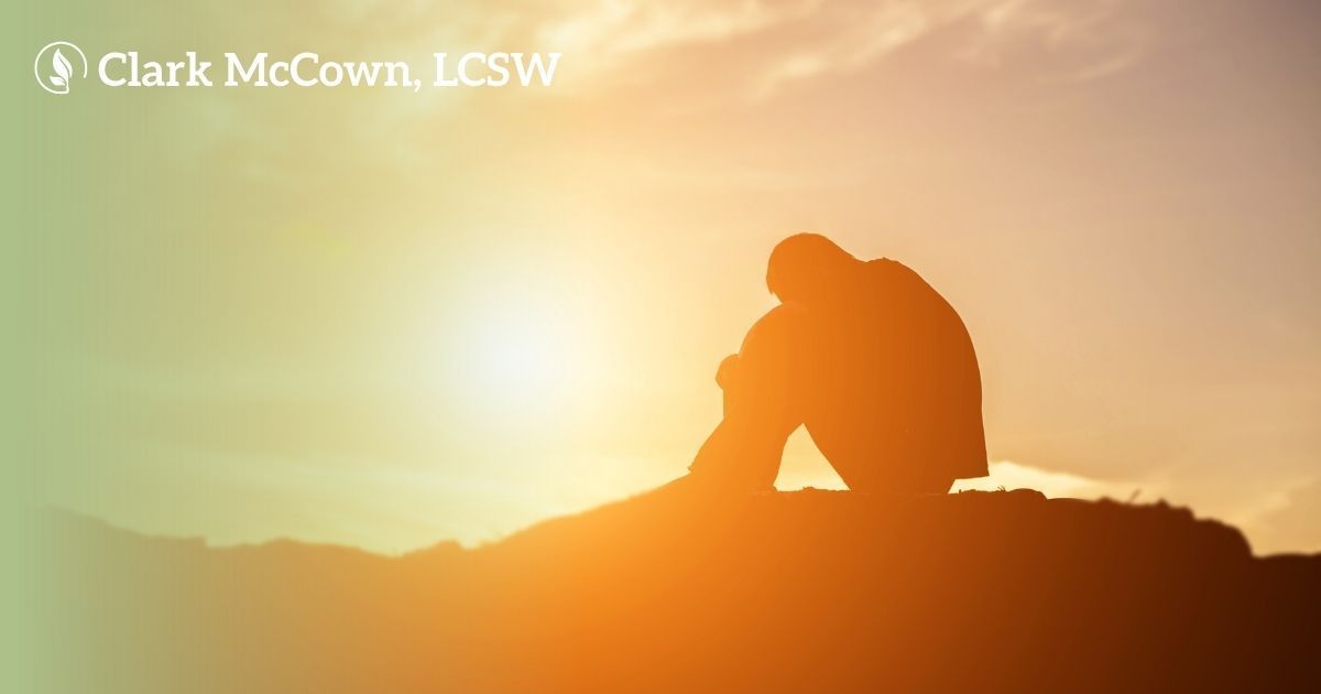 Silhouette of a person sitting on a hill at sunrise, with warm orange light and a bright sun in the sky.