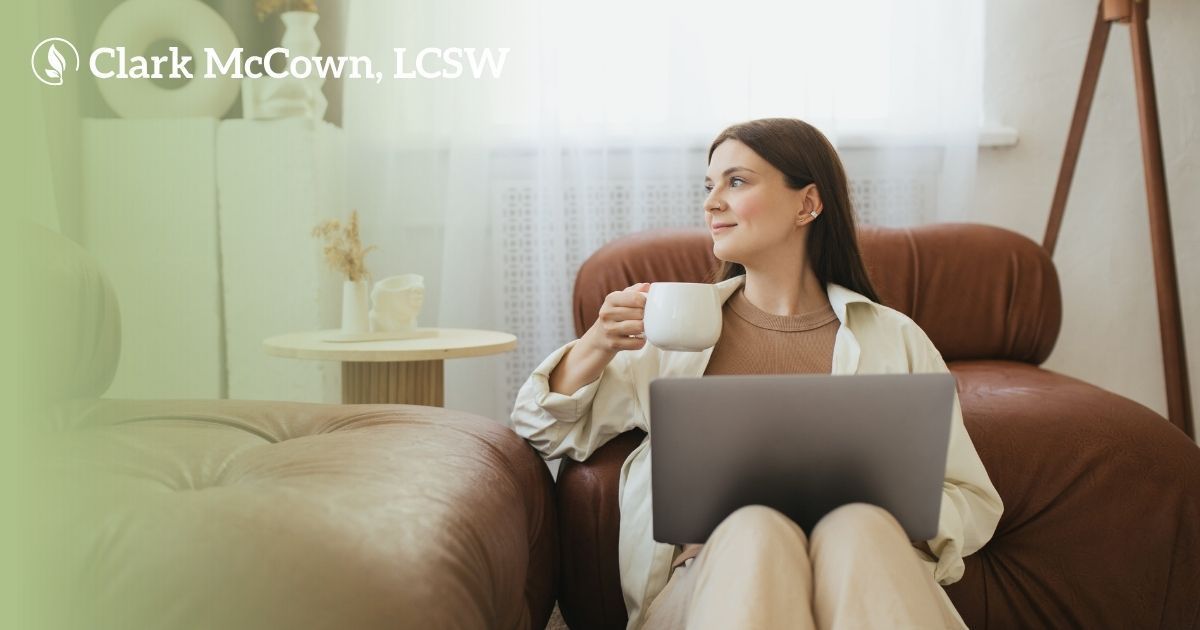 Woman with a laptop and coffee sitting on a brown sofa in a bright living room.