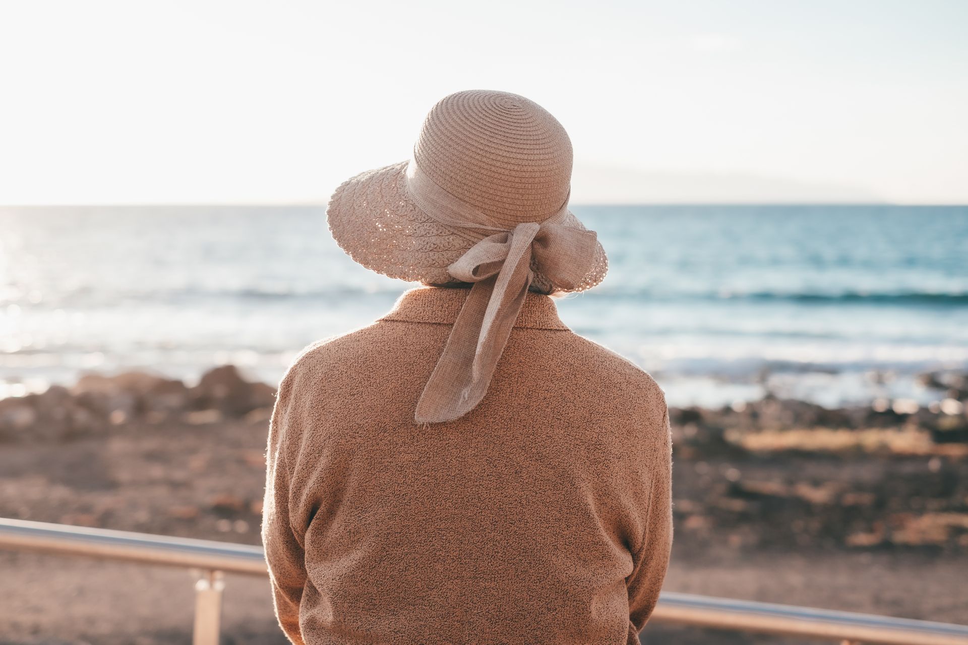 Person in a straw hat facing the ocean at a rocky seaside lookout