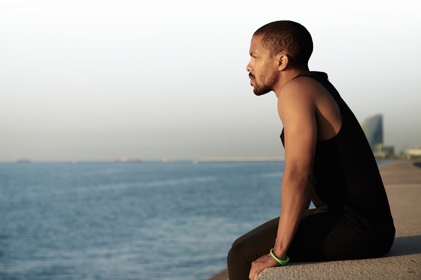 Man sitting on a seawall, looking out over calm water at sunset