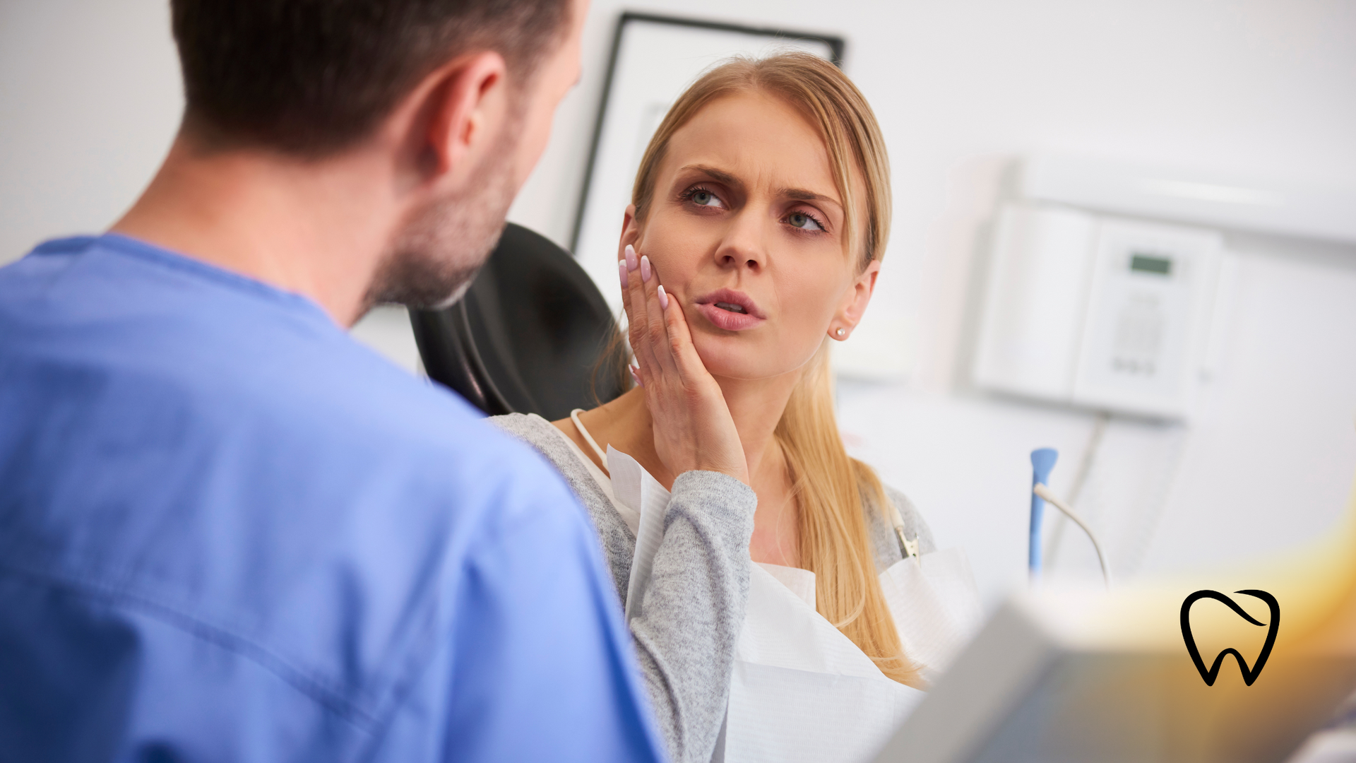 A woman in a dental chair holds her cheek, looking distressed, while a dentist consults her.