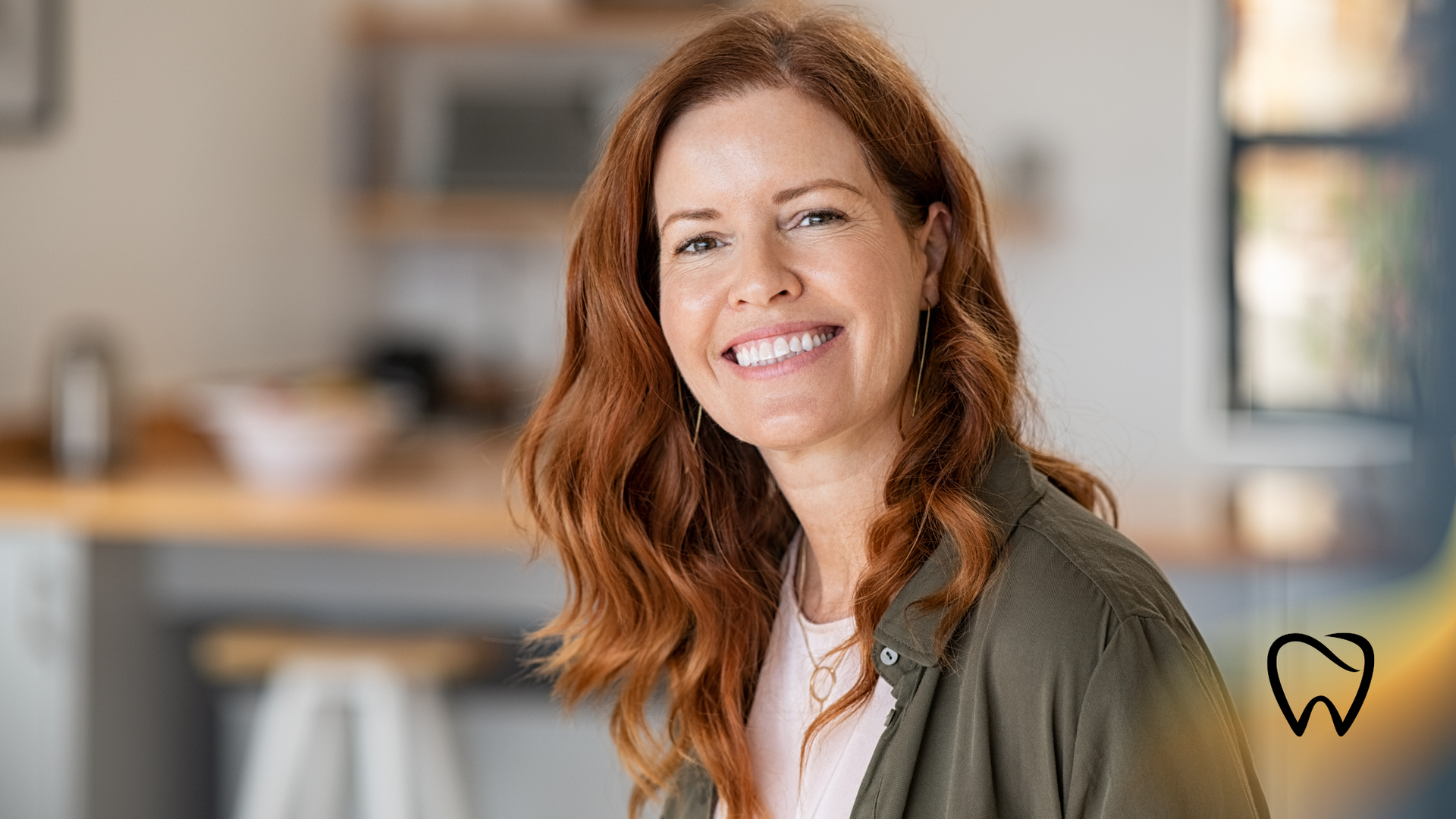 Woman with red hair smiling indoors; soft focus background of a kitchen.