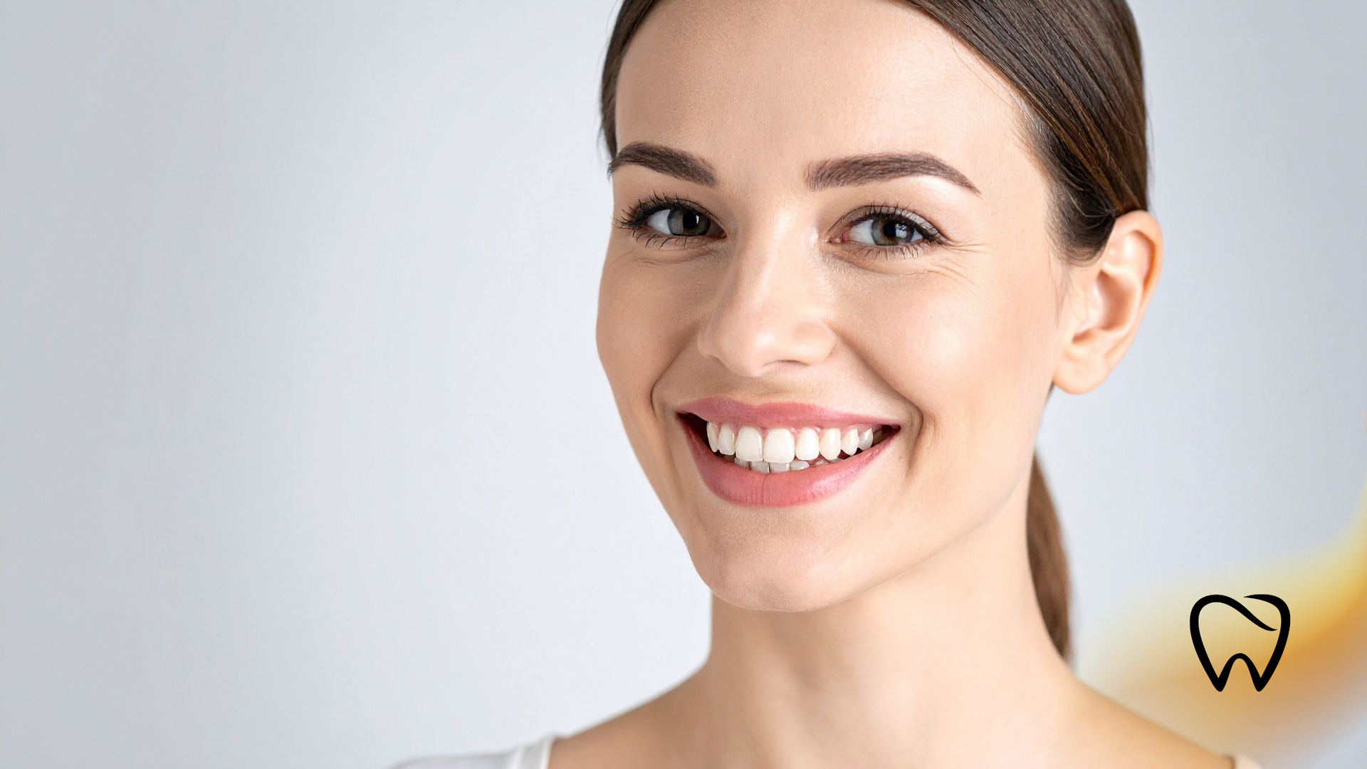 Smiling woman with neatly tied hair on a light gray background, with a small tooth icon in the corner