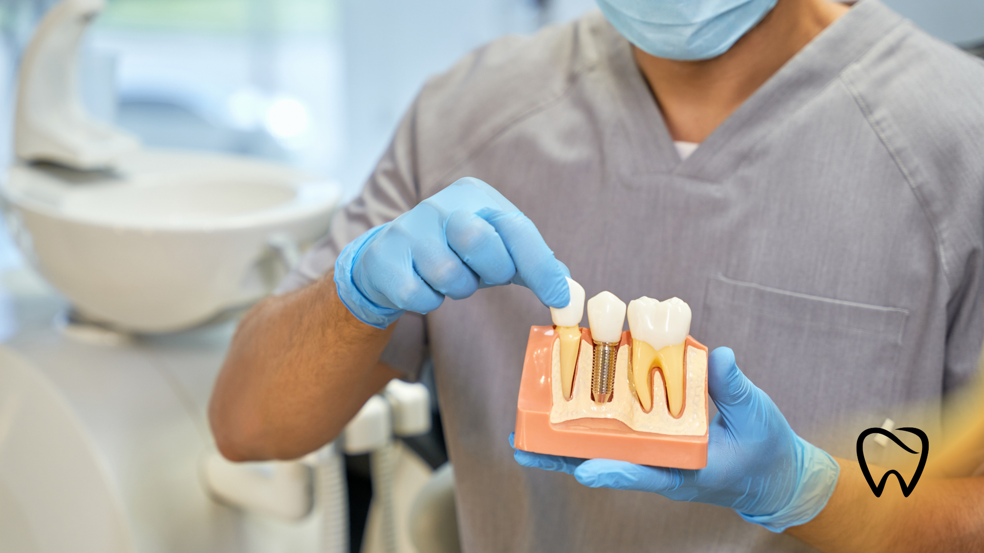 Dentist in scrubs and gloves points to a dental implant model in a clinic setting.