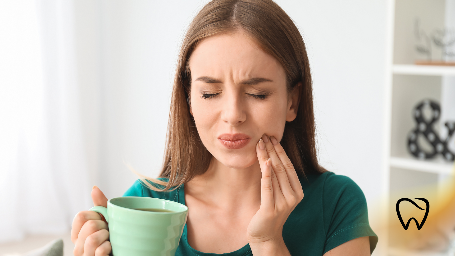 Woman with pained expression, holding a mug, touching her jaw, indoors.