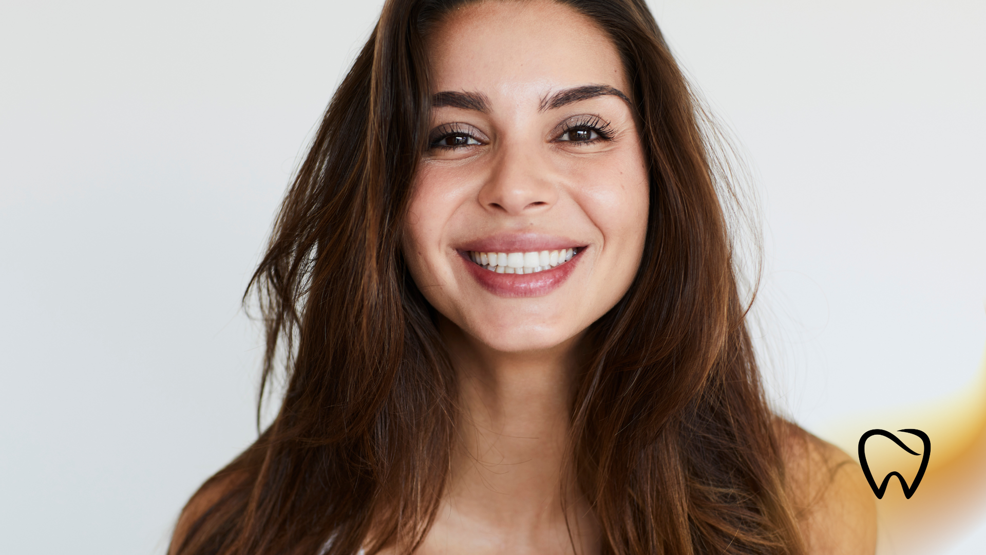 Smiling woman with long brown hair against a light background, with a small logo in the bottom right.