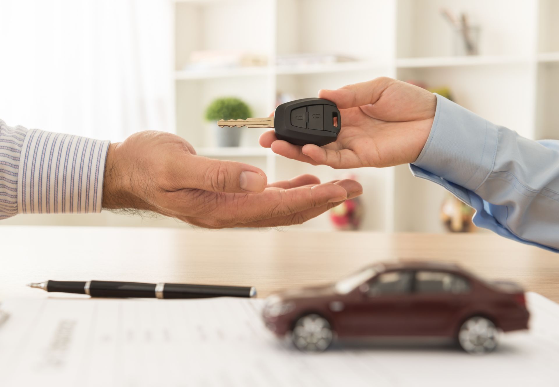 Handing over car keys above a model car and pen on a desk Handing over car keys above a model car and pen on a desk