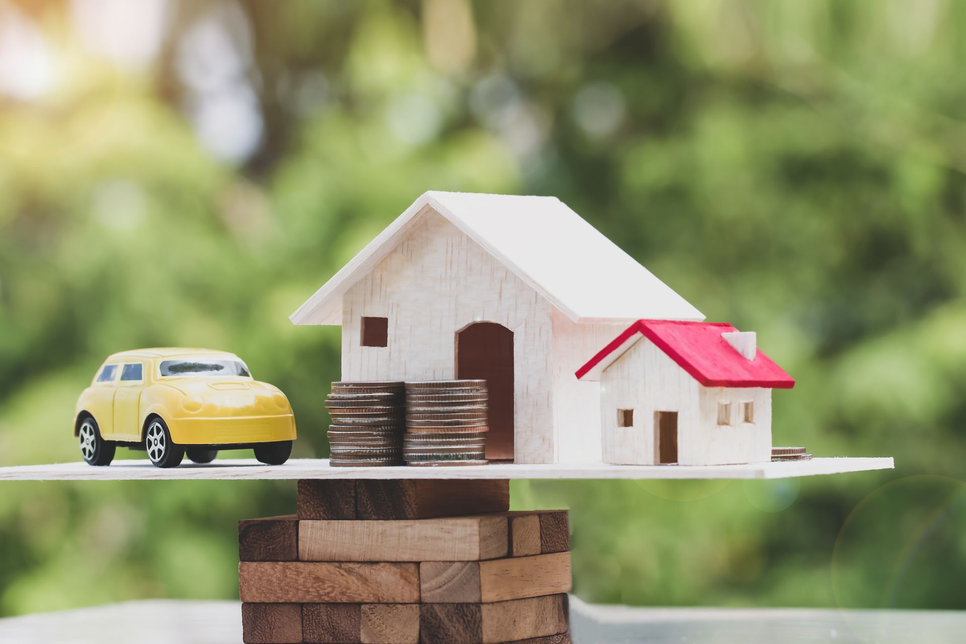Toy car and model houses balanced on stacked coins, symbolizing home and auto insurance. Toy car and model houses balanced on stacked coins, symbolizing home and auto insurance.