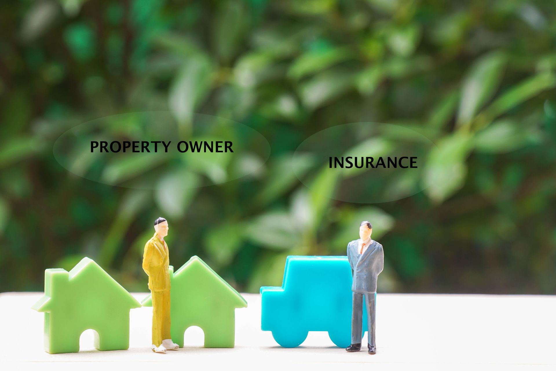 Property owner and insurer beside house models and a blue car on a desk Property owner and insurer beside house models and a blue car on a desk
