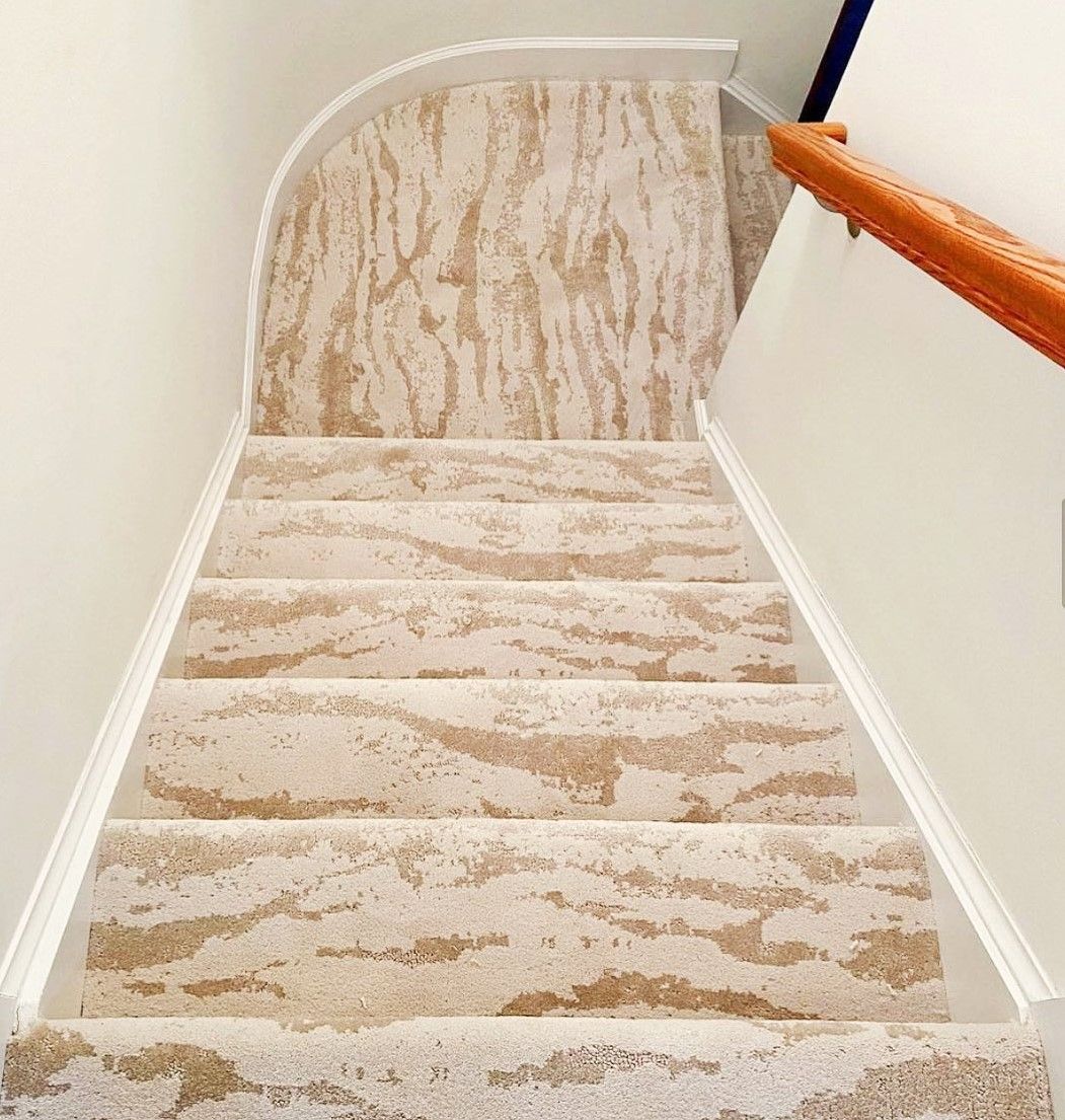 Carpeted staircase with white walls and an orange wooden handrail, viewed from the top.
