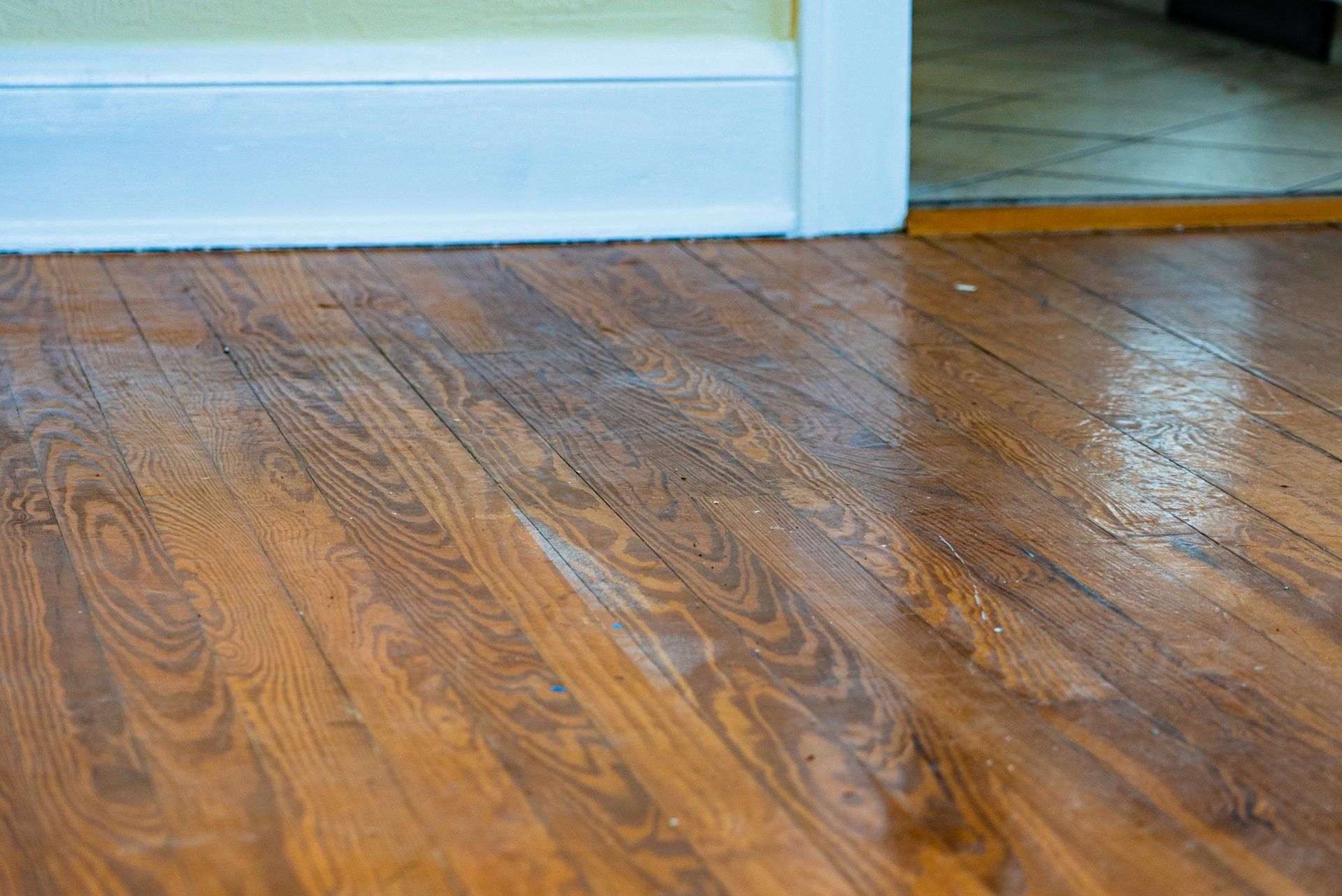 Shiny hardwood floor beside a white baseboard and doorway