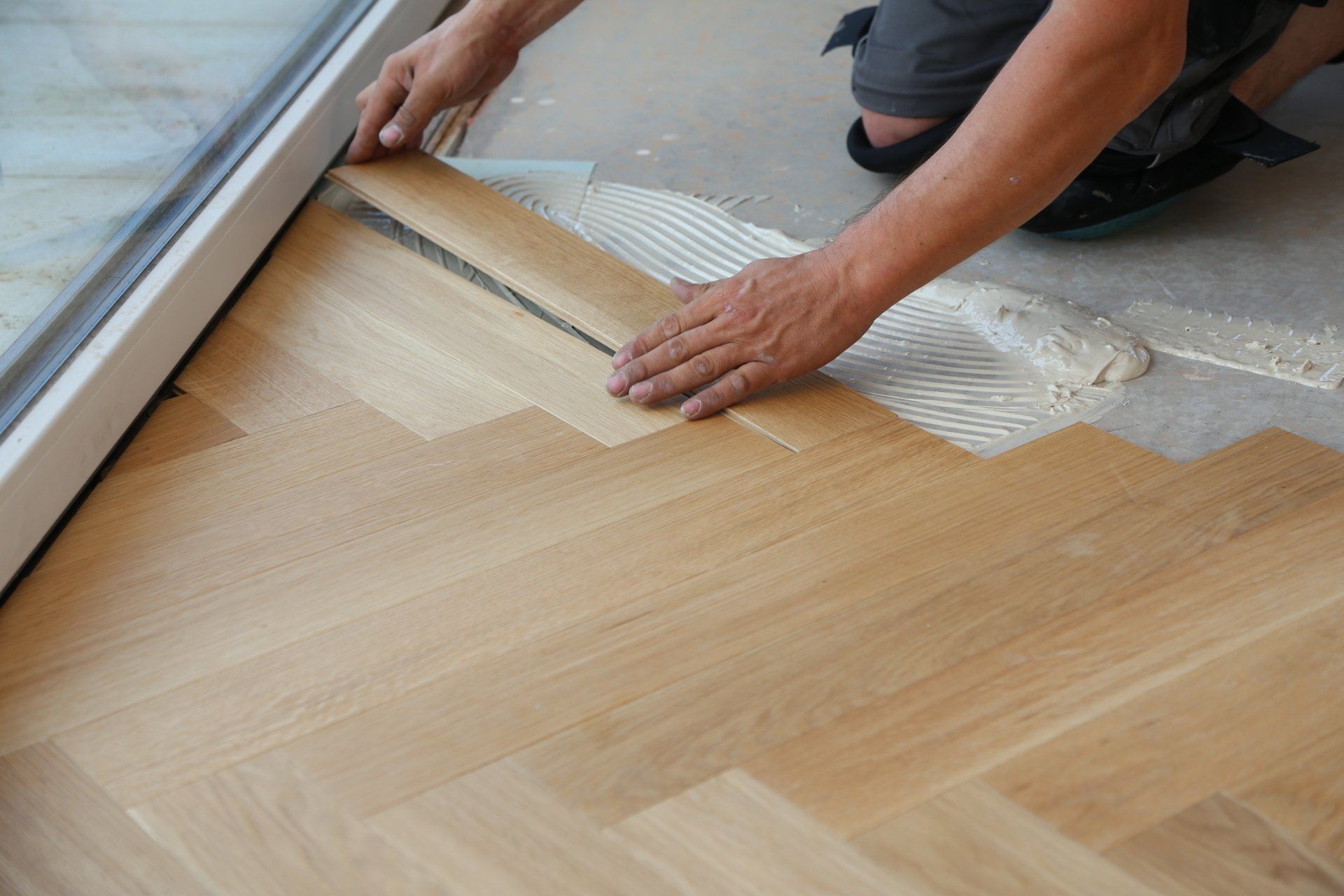 Person laying herringbone wood flooring beside a sliding glass door
