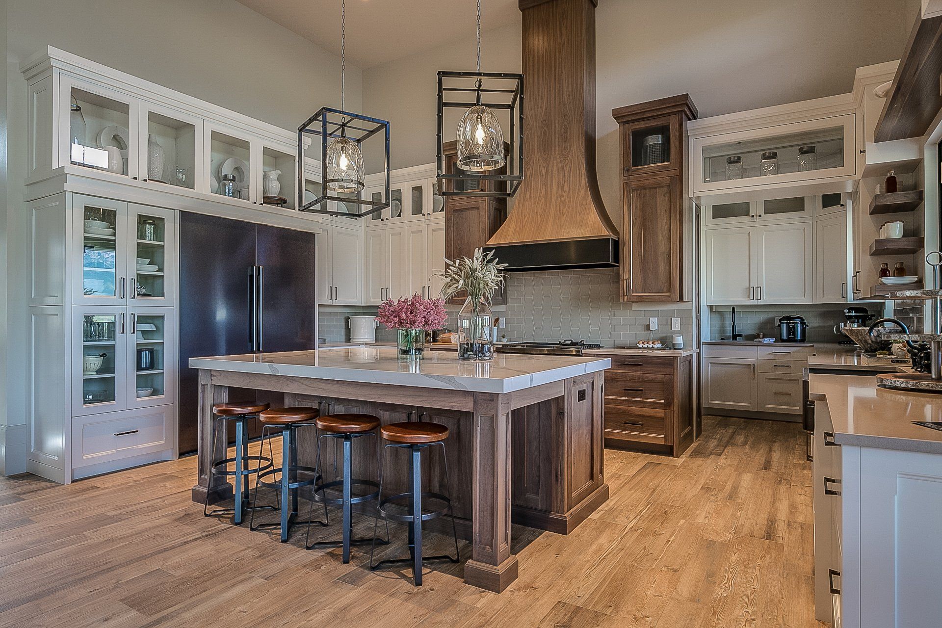Modern kitchen with dark island, black stools, white cabinets, and warm wood floors