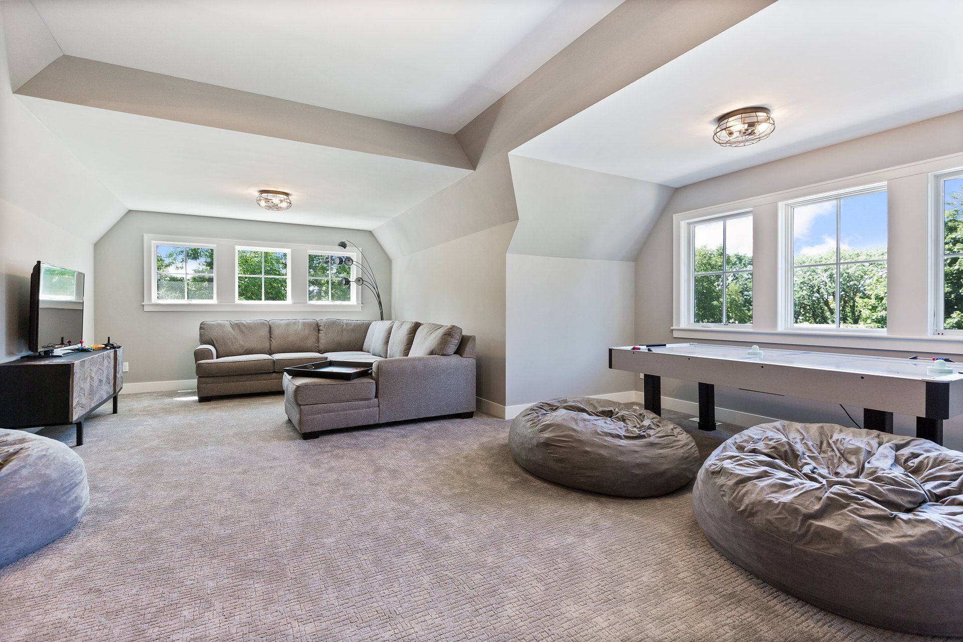 Bright living room with gray sofas, bean bags, and a pool table under sloped ceilings and large windows