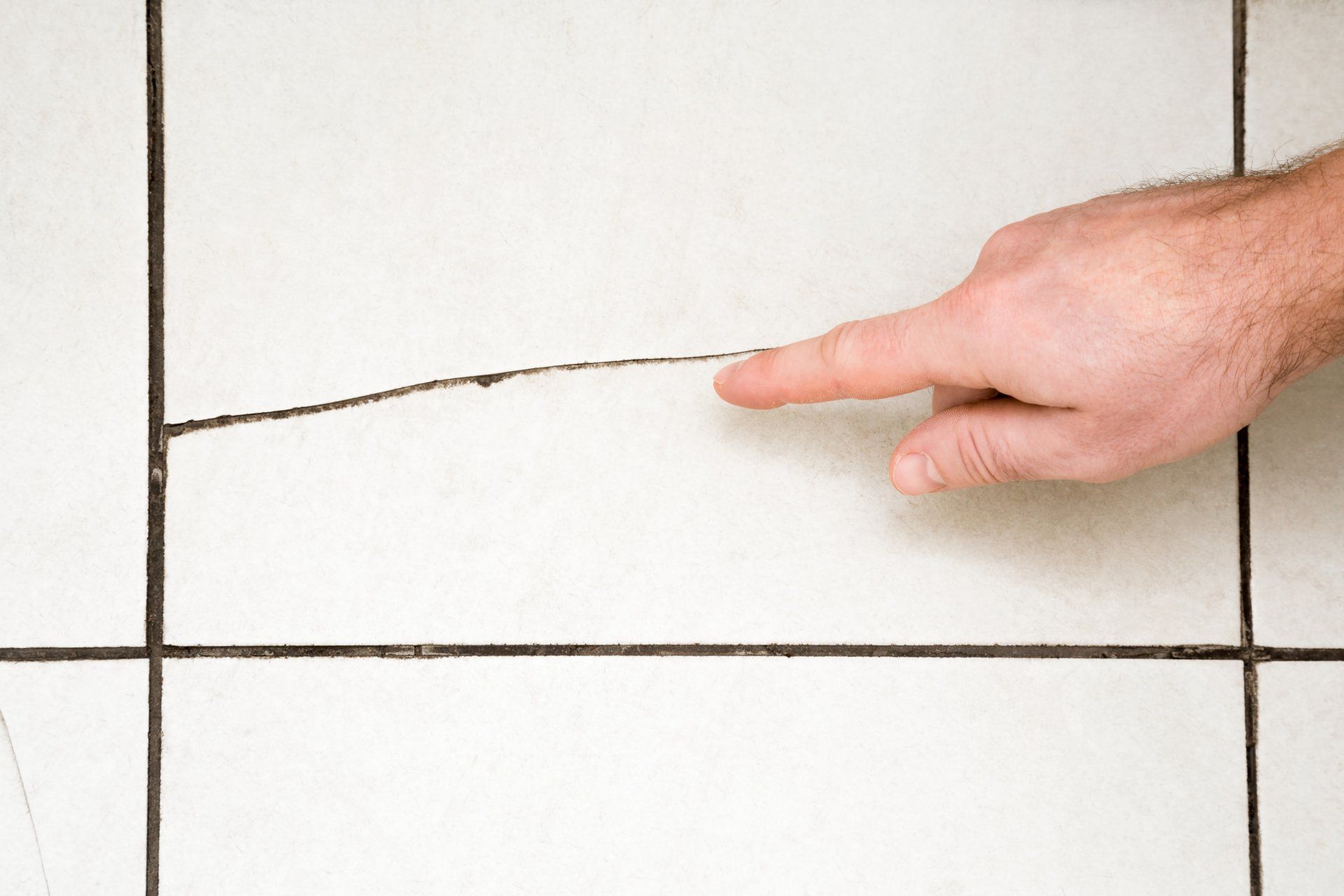 Hand pointing at a crack in a white tiled wall