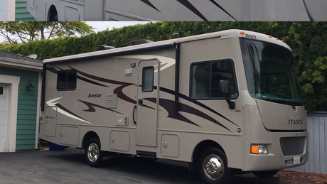 Beige RV parked beside a green garage under palm trees.