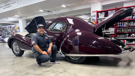 Man kneels beside a maroon vintage car with its hood open in a store aisle