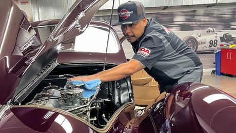 Mechanic working under the open hood of a maroon classic car in a garage