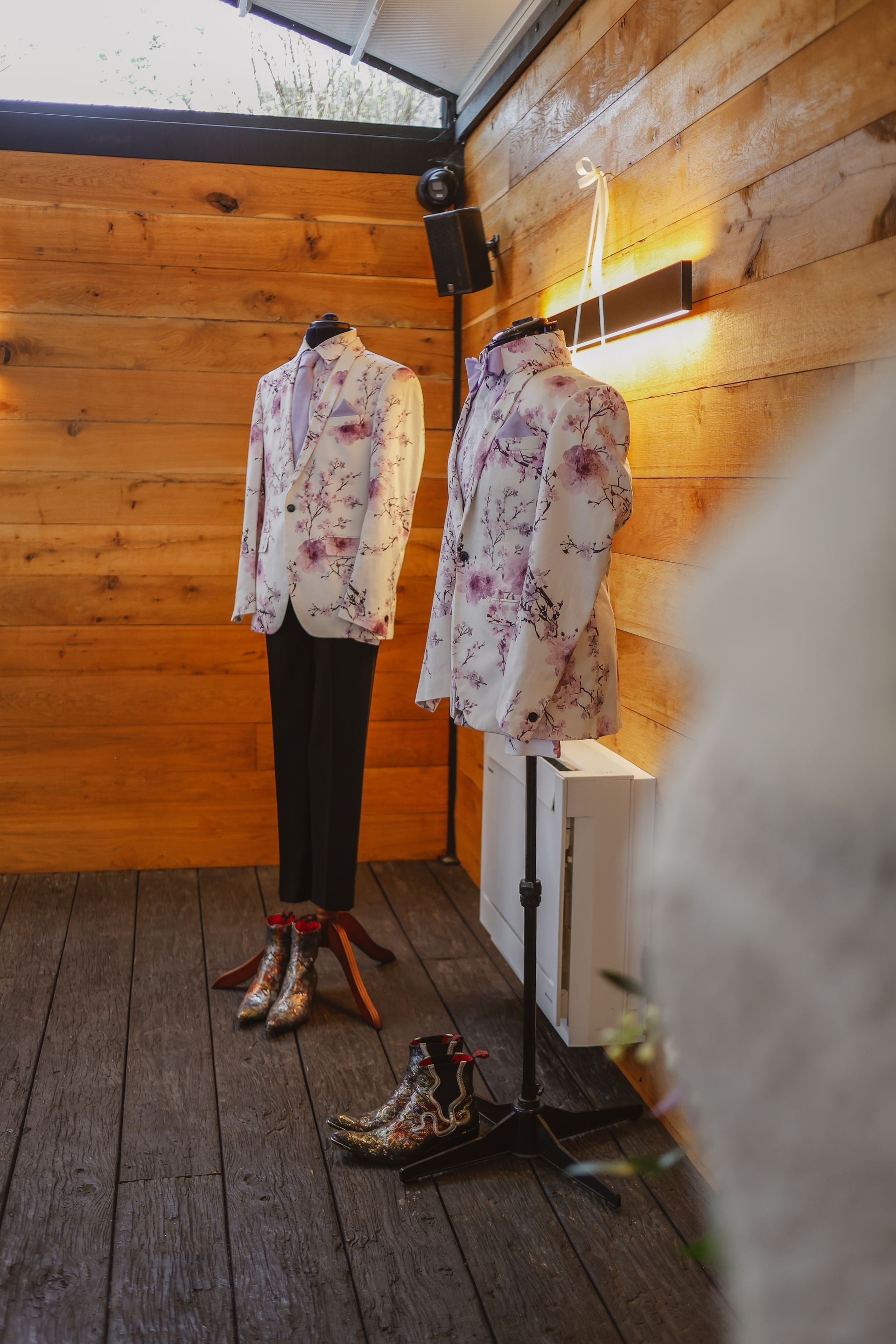 Two patterned shirts on mannequins in a wooden room with a warm wall light.