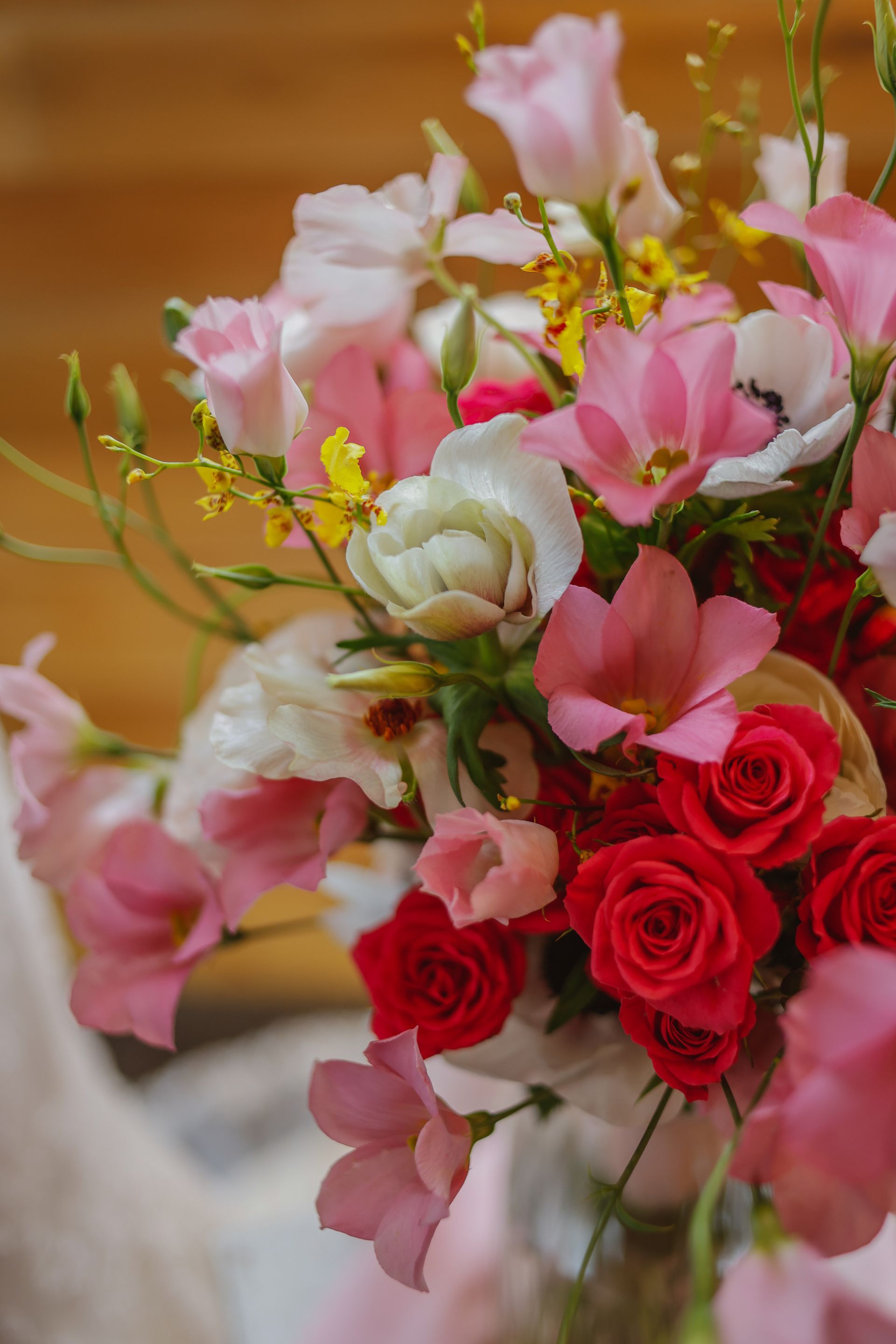 Bouquet of pink and red flowers with white blooms, arranged in a vase against a warm blurred background
