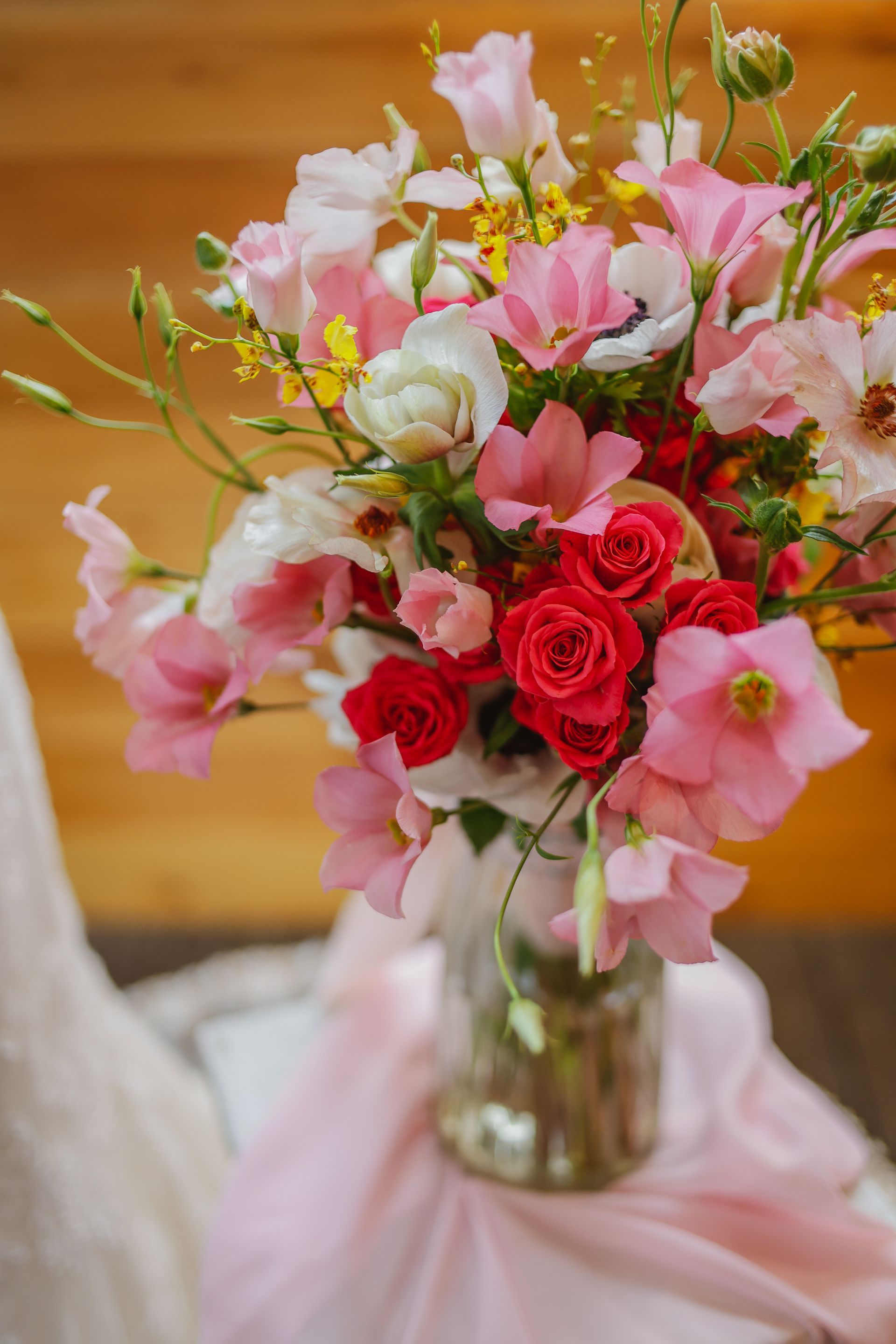 Pink and red floral centerpiece in a glass vase on a draped table