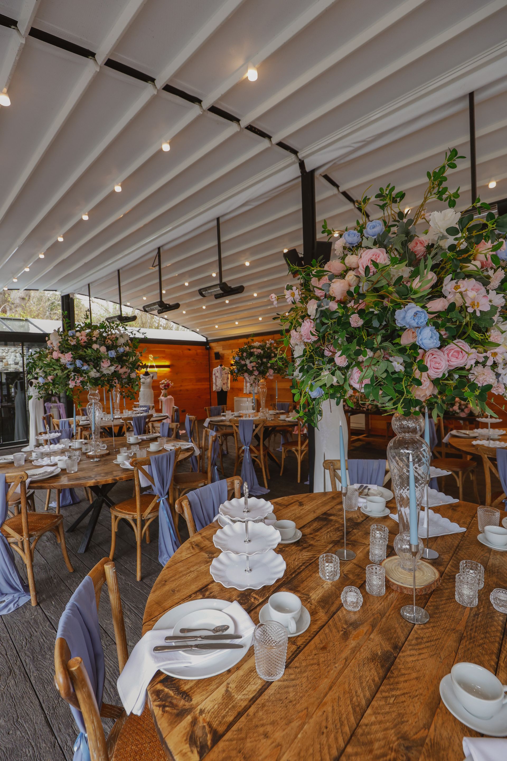 Elegant banquet hall with floral centerpieces, wooden tables, and hanging lights under a white-beamed ceiling