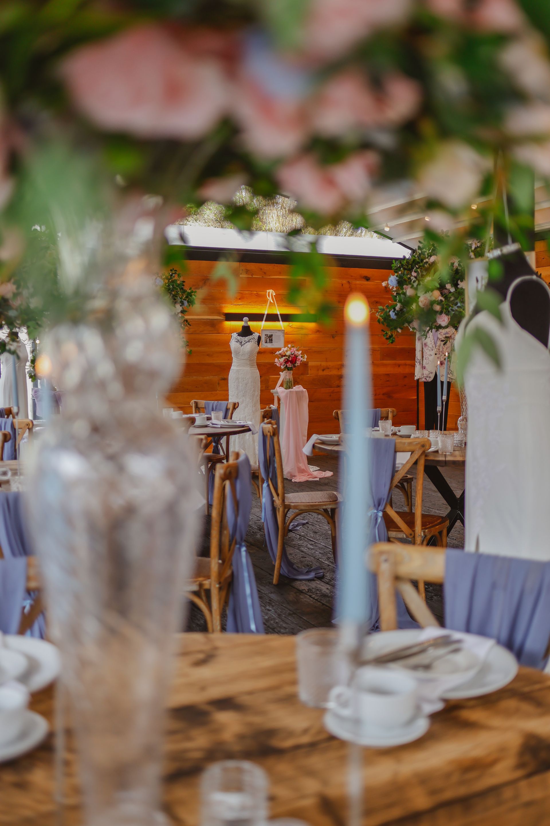 Rustic outdoor dining setup with wooden tables, candles, and blurred flowers in the foreground