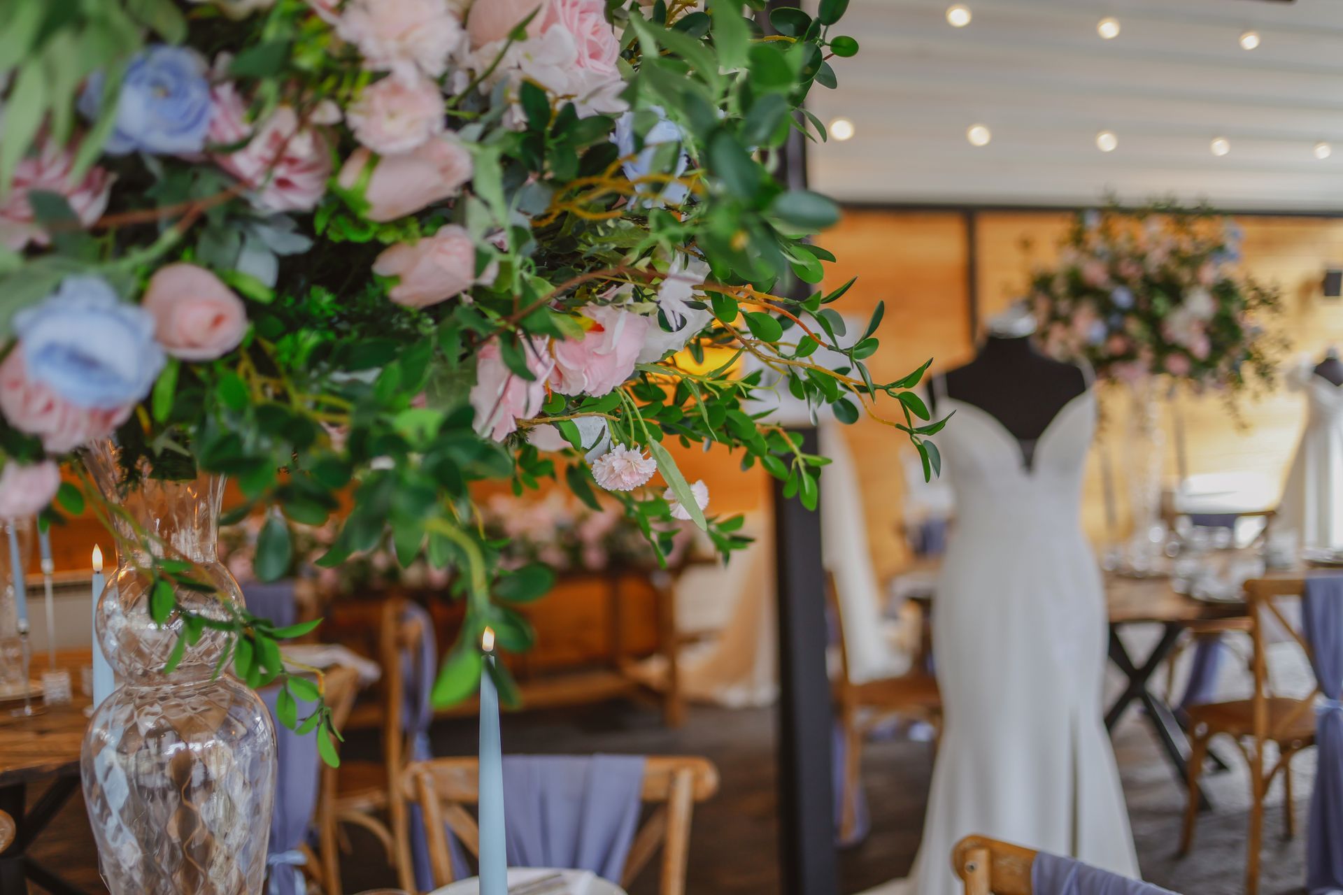 Floral wedding reception table with pink blooms, white chairs, and a wedding dress display in the background