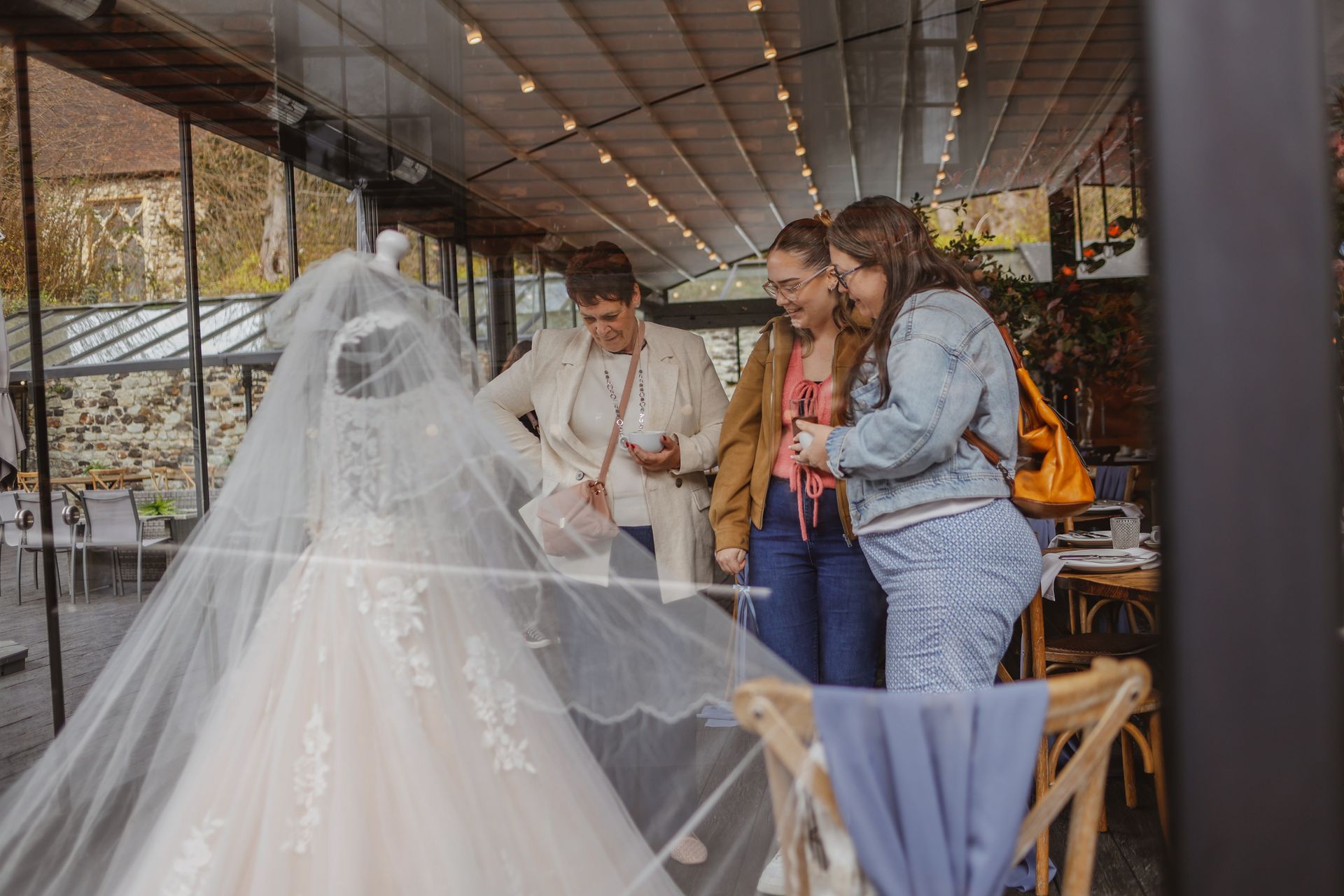 Bride in white veil at decorated outdoor wedding reception, with guests gathered nearby.
