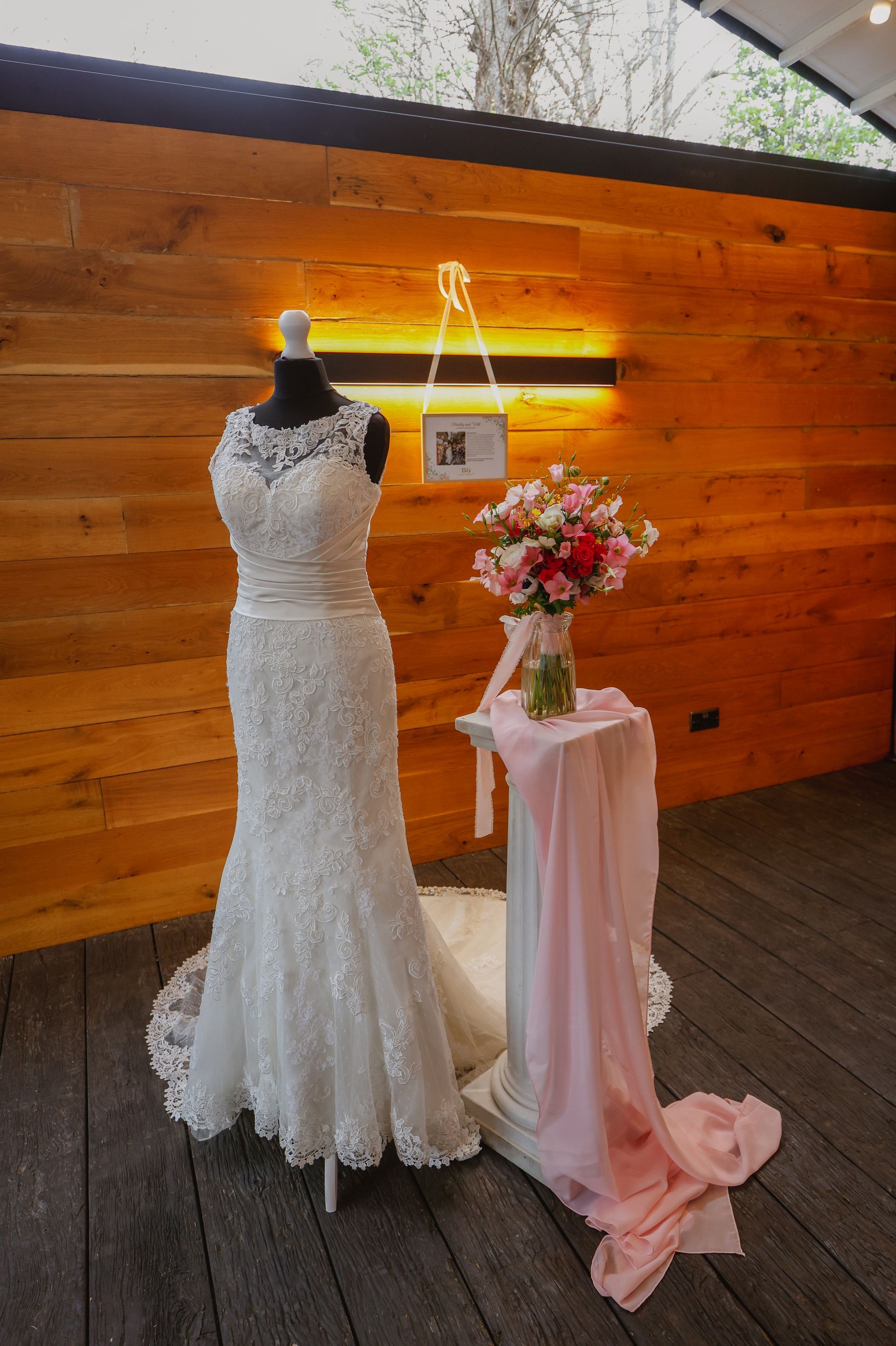 Person in a white lace dress arranging a floral centerpiece beside a pink-draped table against a wooden wall
